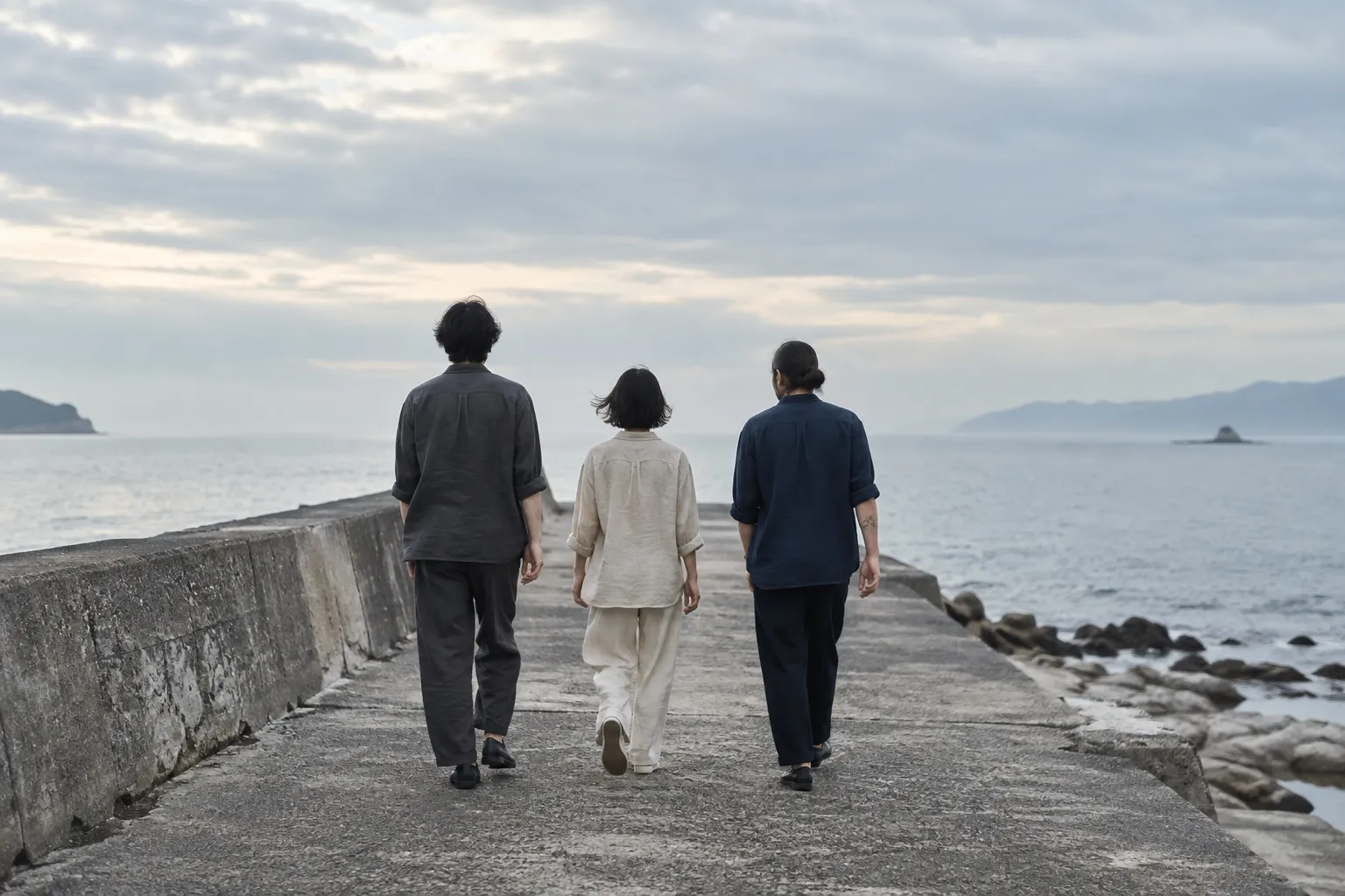 穏やかな海に向かって歩く、藍色とサンド色の服を着た3人の後ろ姿（イメージ）
